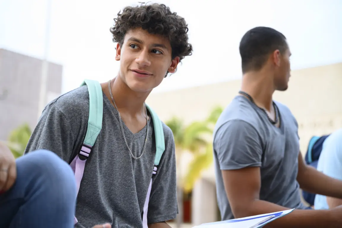 Curly haired teenage Hispanic boy sitting outdoors and visiting with friends in between high school classes.