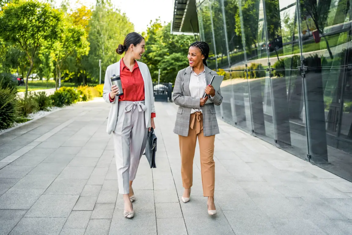 Two cheerful multiracial businesswomen chatting while going to work.