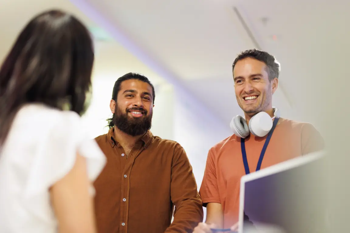 Two male colleagues at being greeted at reception desk of co-working space.