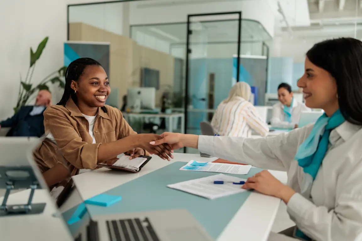 Businesswoman shaking hands with a female client during a successful consultation at her desk in a banking office.